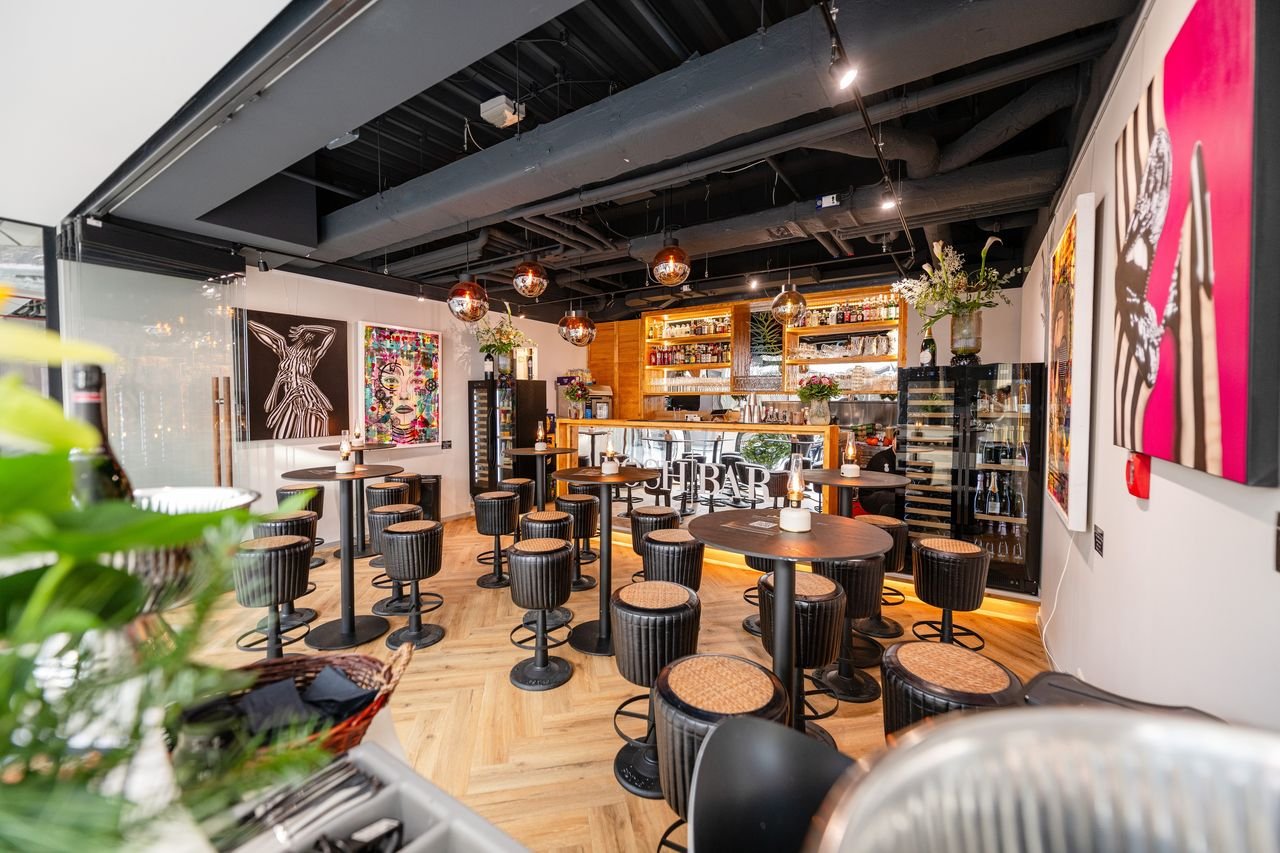 Innenraum der POSH BAR mit Barhockern, Kunstwerken an der Wand und beleuchteter Theke