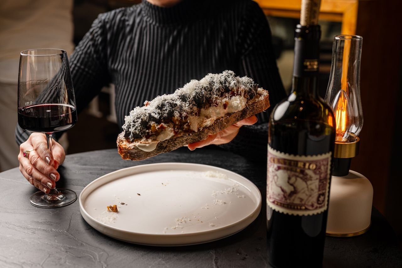 Geröstetes Brot mit Burrata, Gemüse und Trüffel, daneben ein Glas Rotwein