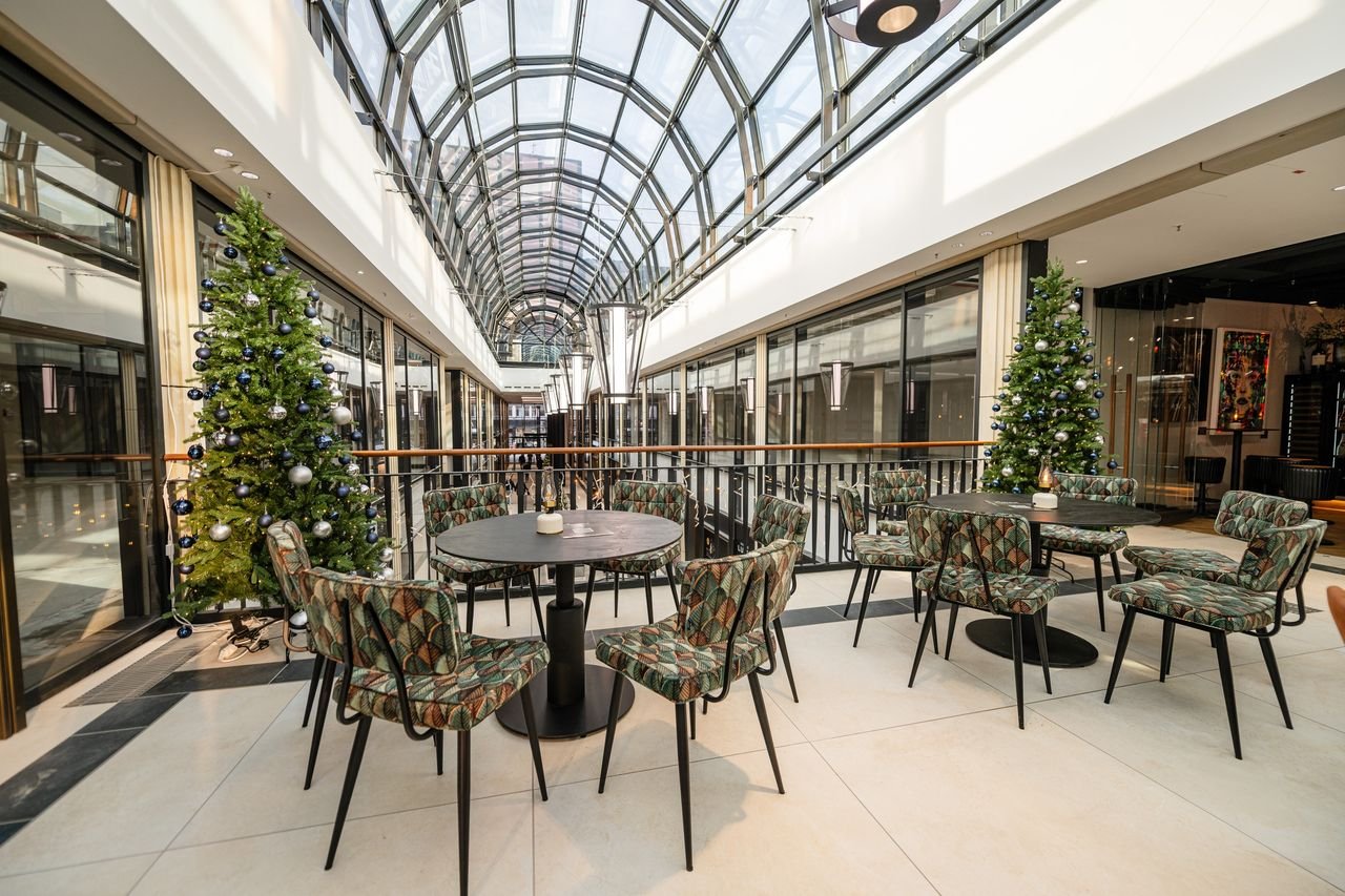 Gedeckte Bistrotische unter dem Glasdach der Galerie Luise, links und rechts geschmückte Weihnachtsbäume