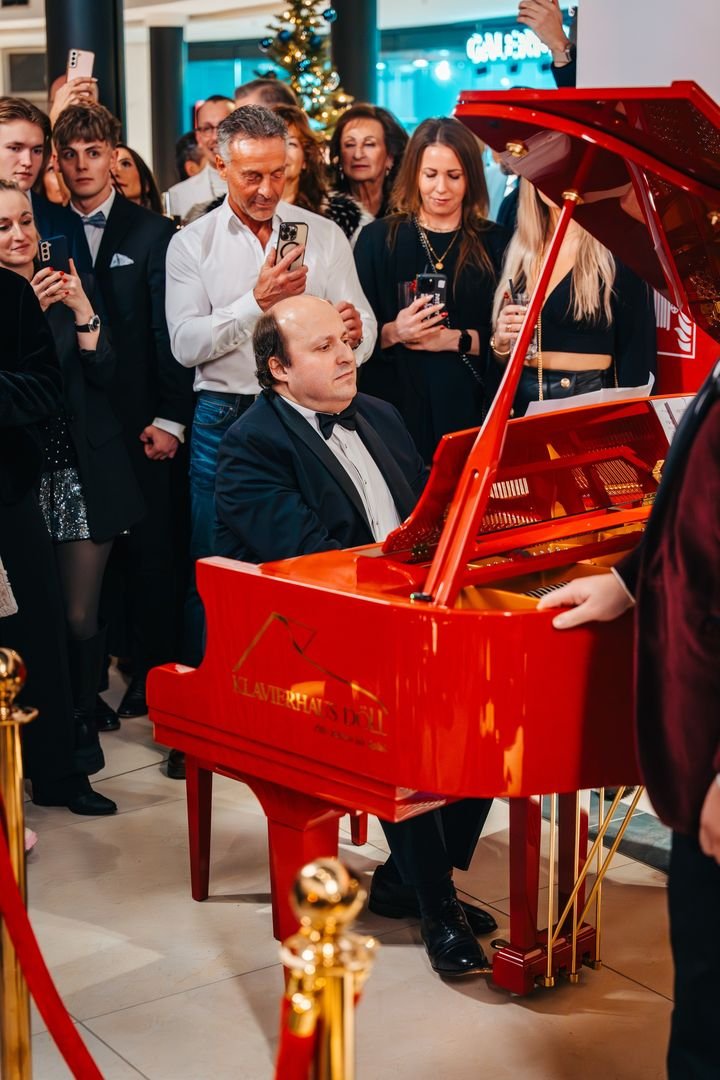 Pianist am roten Flügel, umringt von Gästen mit Smartphones