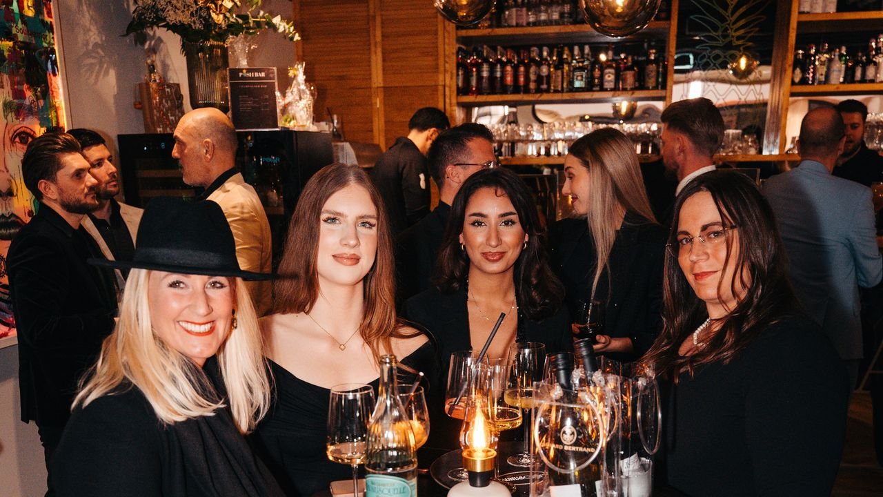 Vier Gäste feiern bei Kerzenlicht an einem Tisch in der POSH BAR, im Hintergrund die beleuchtete Bar