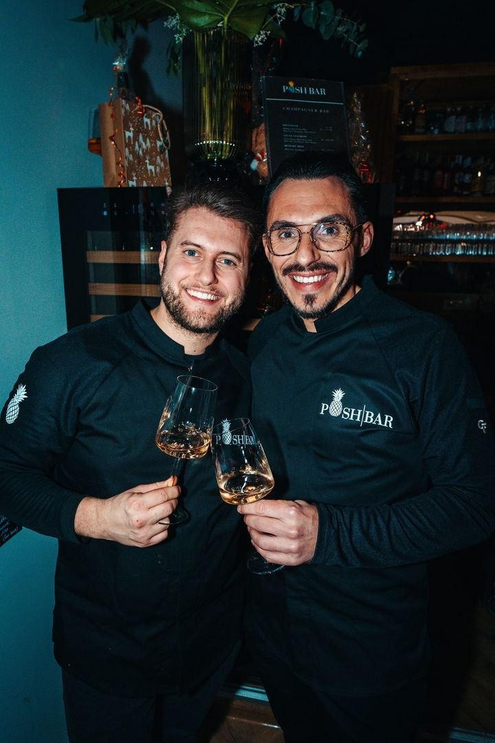 Zwei Mitglieder des POSH BAR Teams stoßen mit Weißwein an